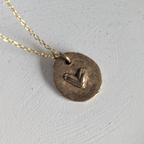 Gold necklace with a round pendant on a white dish, with dried flowers in the background.