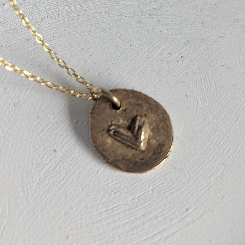 Gold necklace with a round pendant on a white dish, with dried flowers in the background.