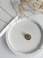 Gold necklace with a round pendant on a white dish, with dried flowers in the background.