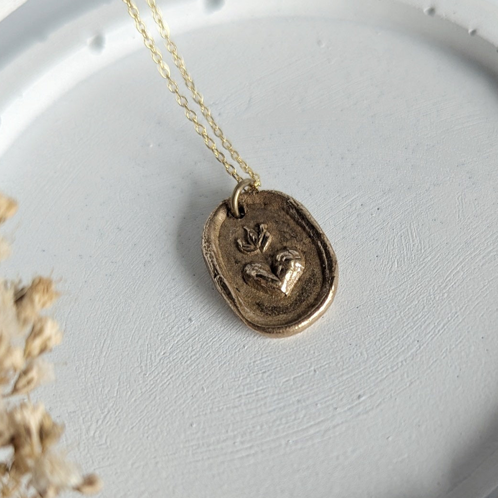 Gold necklace with a pendant on a white dish, surrounded by dried flowers.