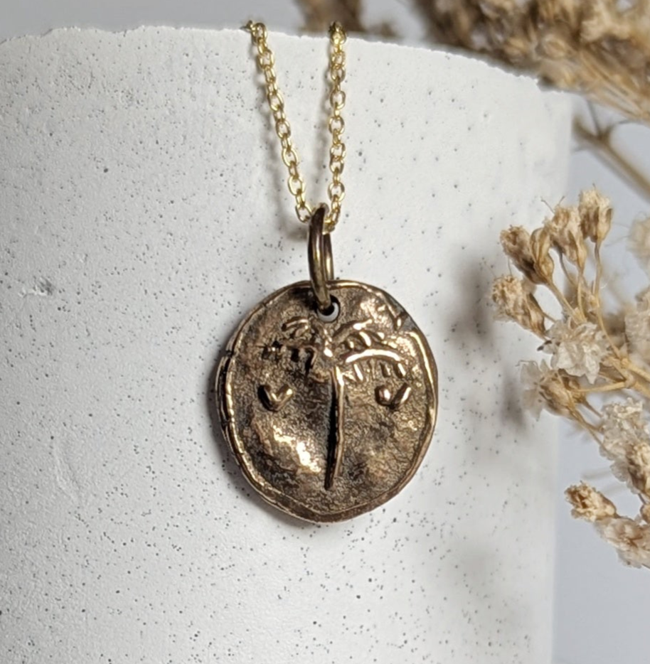 Gold necklace with a pendant on a white cylindrical stand with dried flowers.