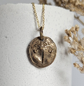 Gold necklace with a pendant on a white cylindrical stand with dried flowers.