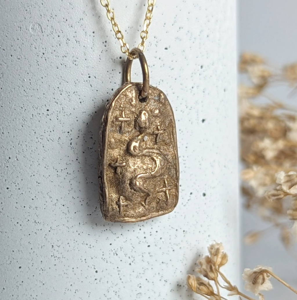 Gold necklace with a pendant on a white surface with dried flowers.
